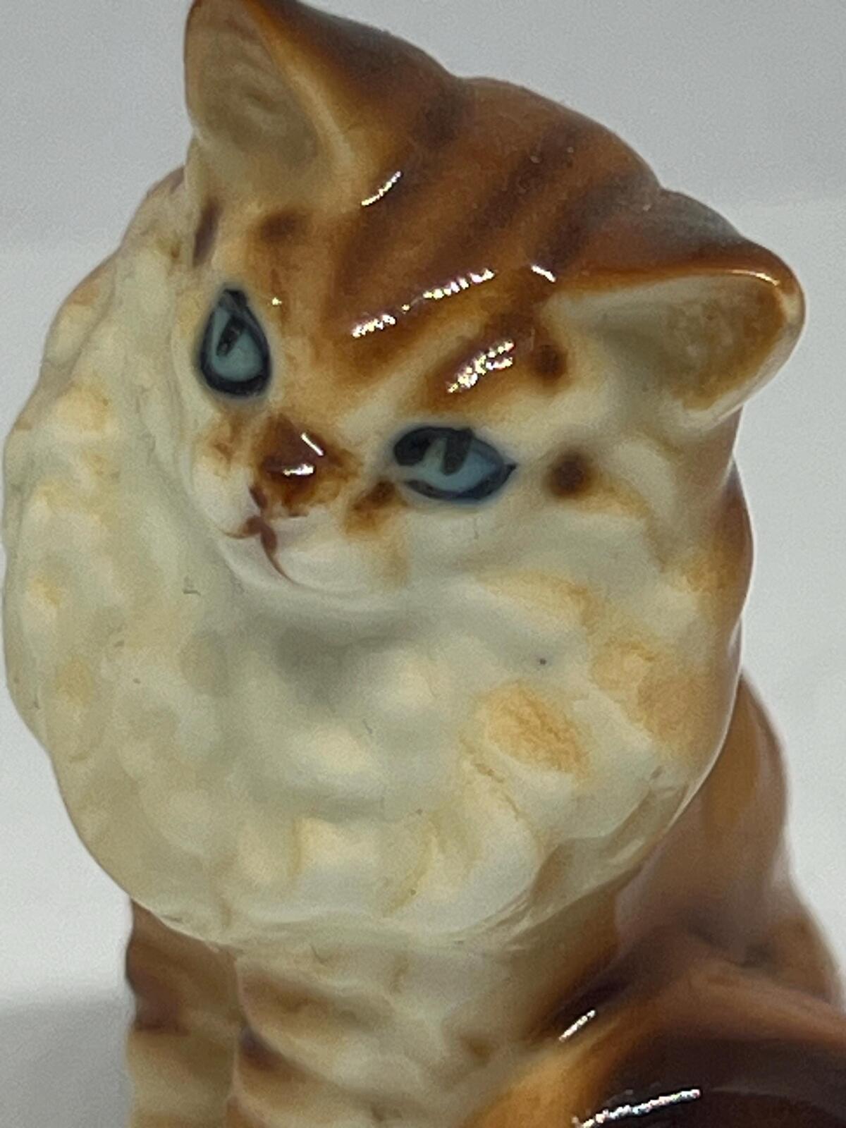 Miniature hand-painted porcelain cat figurine with blue eyes and a tabby calico pattern.