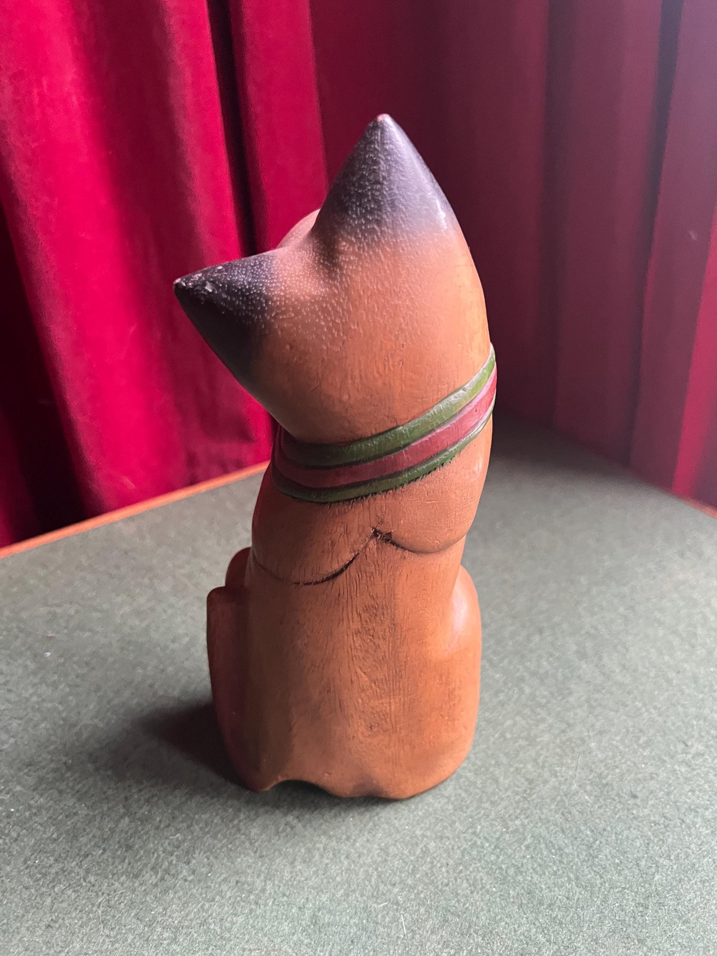 Quirky head tilted Siamese cat with red green collar. Rustic wooden kitten sculpture.