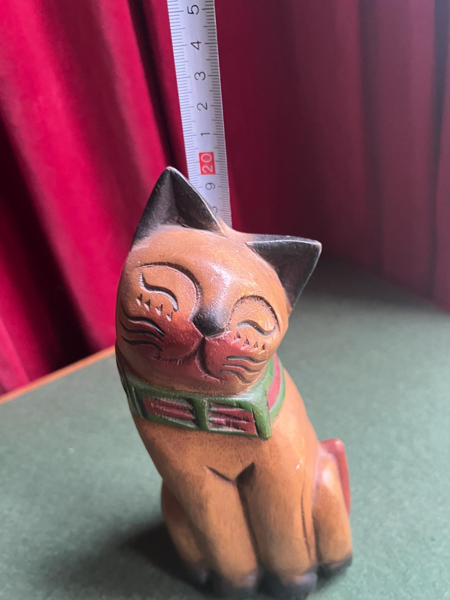 Quirky head tilted Siamese cat with red green collar. Rustic wooden kitten sculpture.
