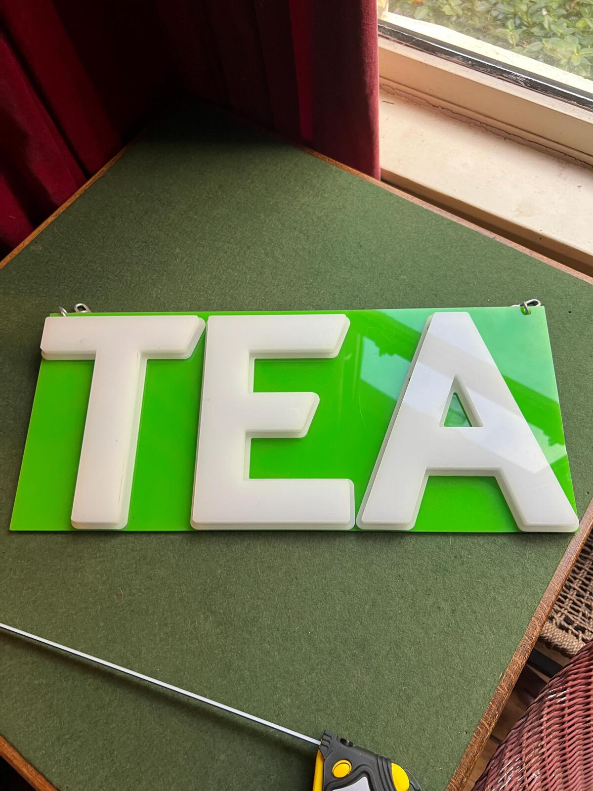 Vintage plastic TEA sign. White plastic letters on neon green background. Silver metal hanging chain.