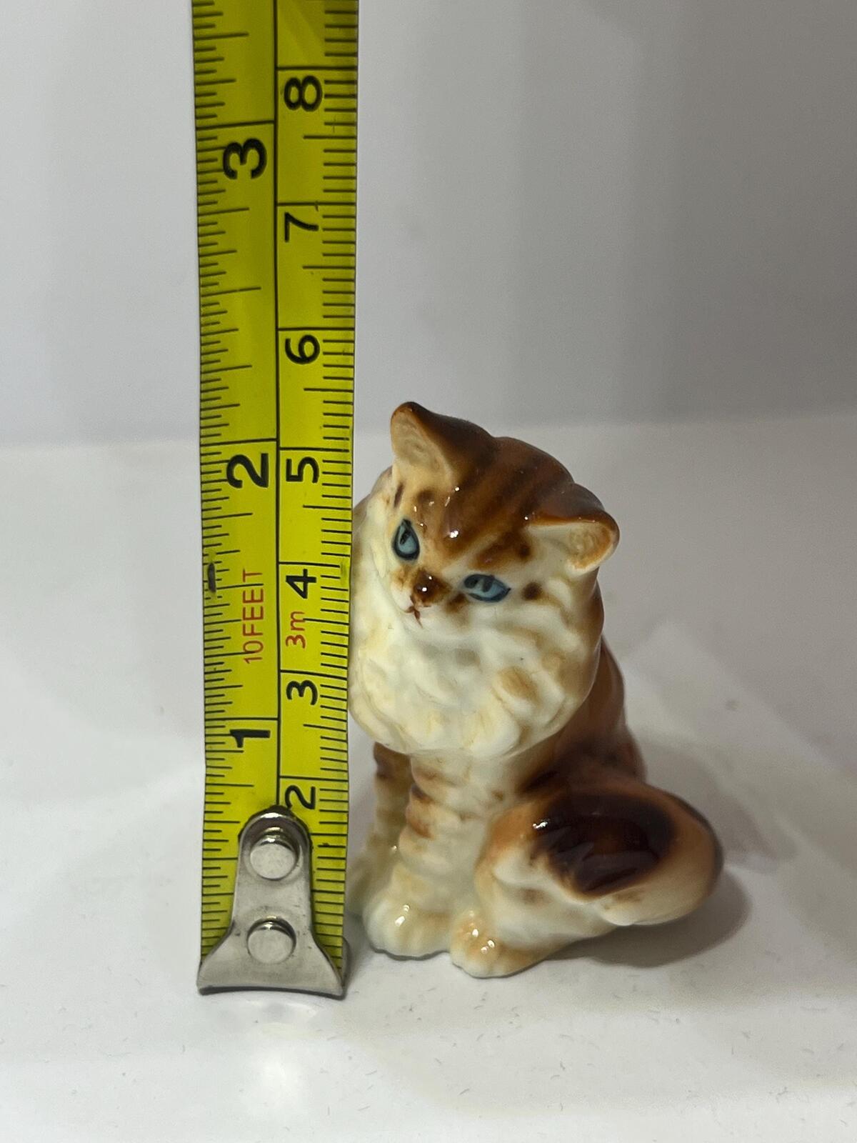 Miniature hand-painted porcelain cat figurine with blue eyes and a tabby calico pattern.