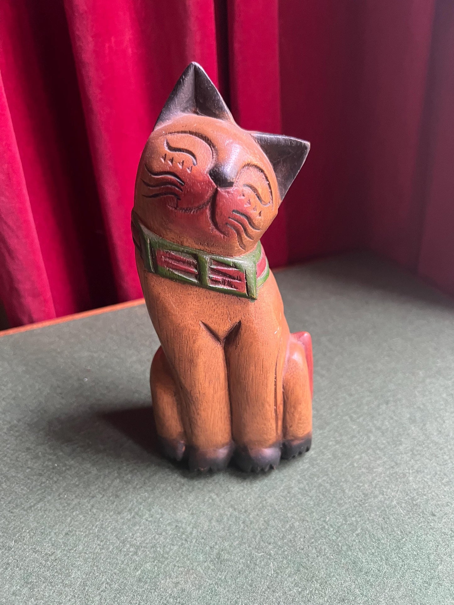 Quirky head tilted Siamese cat with red green collar. Rustic wooden kitten sculpture.