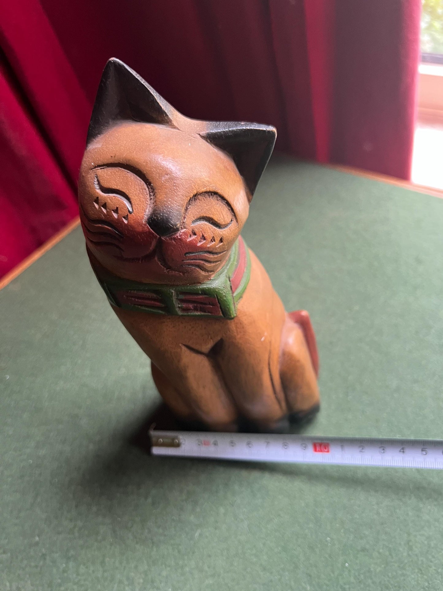 Quirky head tilted Siamese cat with red green collar. Rustic wooden kitten sculpture.