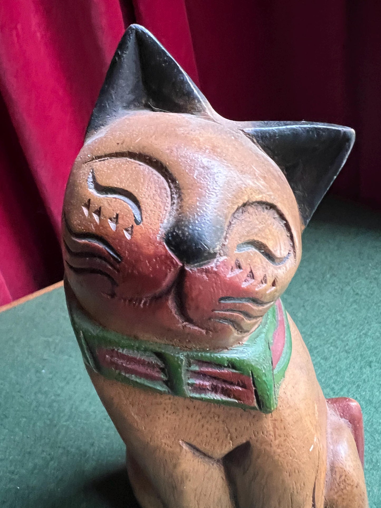 Quirky head tilted Siamese cat with red green collar. Rustic wooden kitten sculpture.