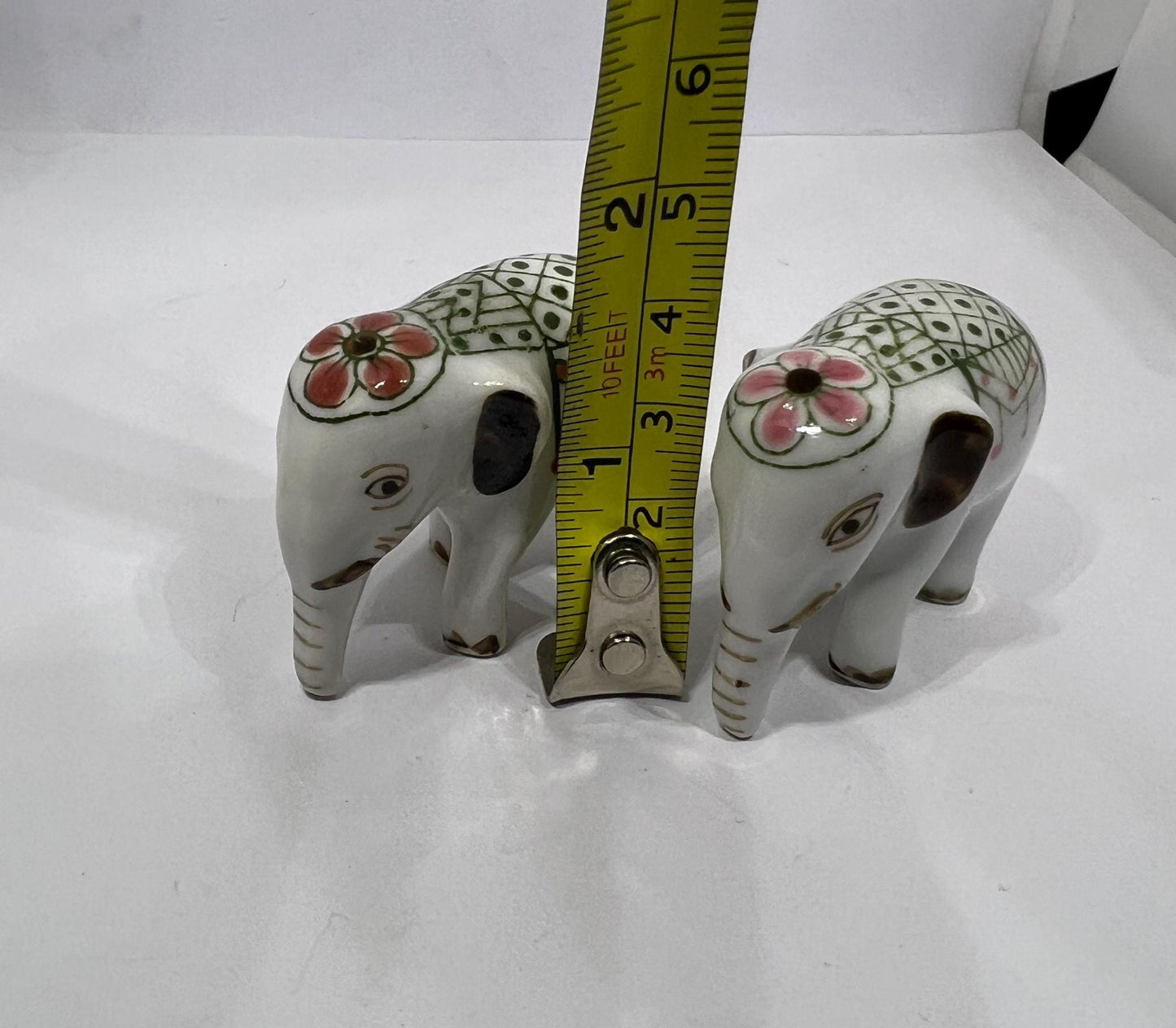 Tiny pair ceramic elephants in ceremonial dress with floral head dress.